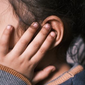 A young girl with long dark hair covering her ear in a thoughtful pose.